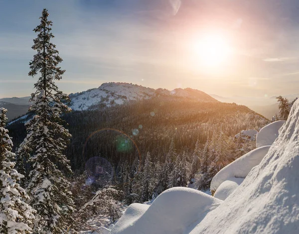Schöne ländliche Winterlandschaft mit der untergehenden Sonne über dem Berg, den schneebedeckten Wäldern und Felsen — Stockfoto