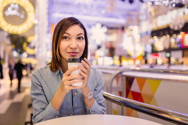 Portrét krásné roztomilé dívce sedící s kávou odnést v nákupní centrum zdobené pro nový rok — Stock fotografie