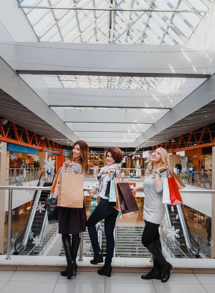 Drie mooie jonge vrouwen met boodschappentassen kijken camera in het winkelcentrum — Stockfoto