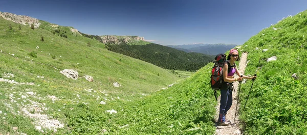 Pěší turistika mladá žena s batohem a trekingové hůlky na horské stezce — Stock fotografie