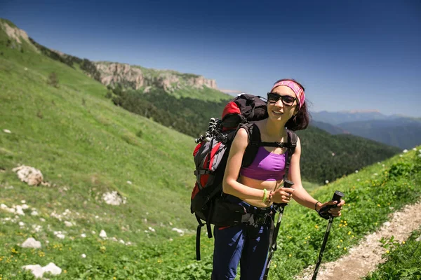 Пешая молодая женщина с рюкзаком и палками на горной тропе — стоковое фото