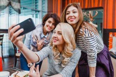 Üç mutlu sevimli kız arkadaş Cafe içinde alarak Selfie. Modern dostluk ve kadınlar arasındaki ilişkileri kavramı