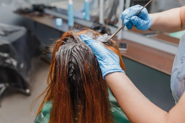 No estilista de salão profissional em luvas com pincel aplicando tinta para o cabelo vermelho brilhante do cliente. O conceito de técnicas de coloração de corantes em Baloyazh — Fotografia de Stock