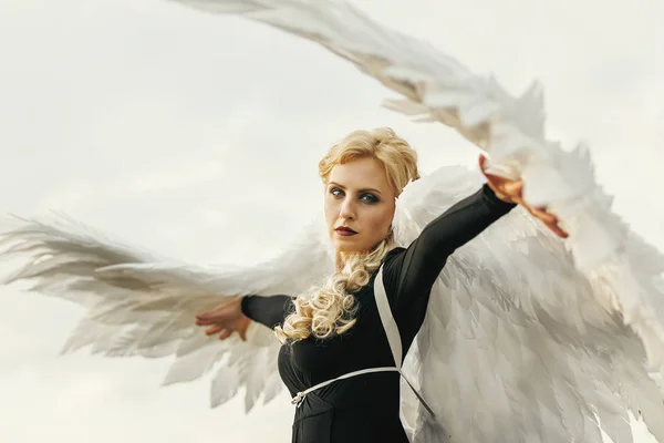 극적인 일몰 하늘 배경에 큰 하얀 천사 날개와 검은 드레스에 젊은 매력적인 여자. 타락 한 다크 엔젤의 개념 — 스톡 사진