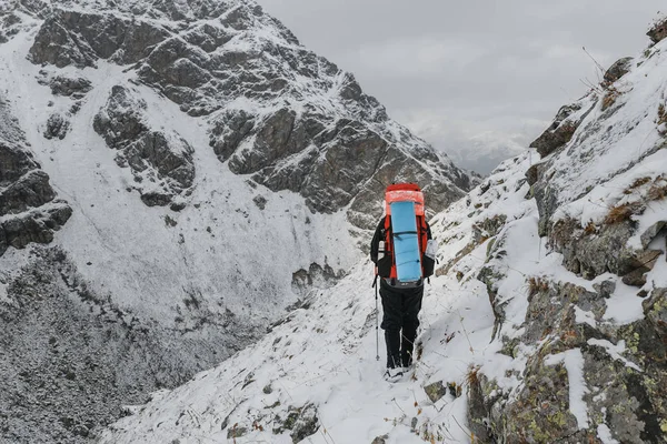 Альпинист ходит по крутому заснеженному склону в горах на фоне скалы и бездны. Концепция риска и приключений на открытом воздухе — стоковое фото