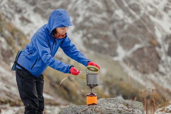 Mulher água fervente em jato de gás de acampamento portátil perto da tenda de caminhadas em montanhas nevadas no final do outono — Fotografia de Stock