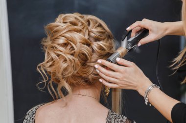 Kuaför bir kadın kumlu saç yüksek moda düğün ya da akşam saç modeli yapar