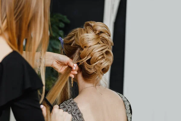 Hairdresser makes upper bun wedding hairstyle close-up on sandy blond hair of beautiful woman — Stock Photo, Image