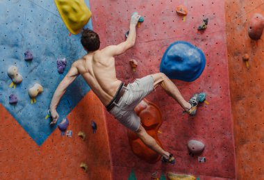 Kas ve formda üstsüz adam egzersiz bouldering ve kapalı yapay duvar tırmanışı