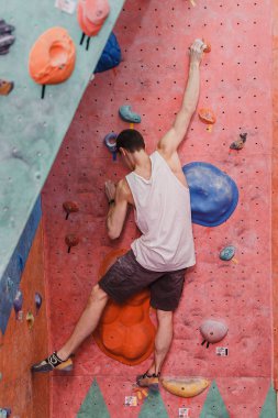 Özgür kapalı yapay kaya tırmanma tırmanıcı genç adam, arkadan görünüm