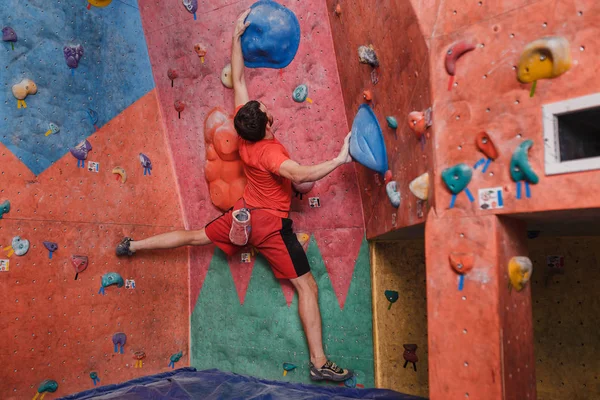 Visão traseira de um jovem praticando na escalada na parede artificial no ginásio — Fotografia de Stock