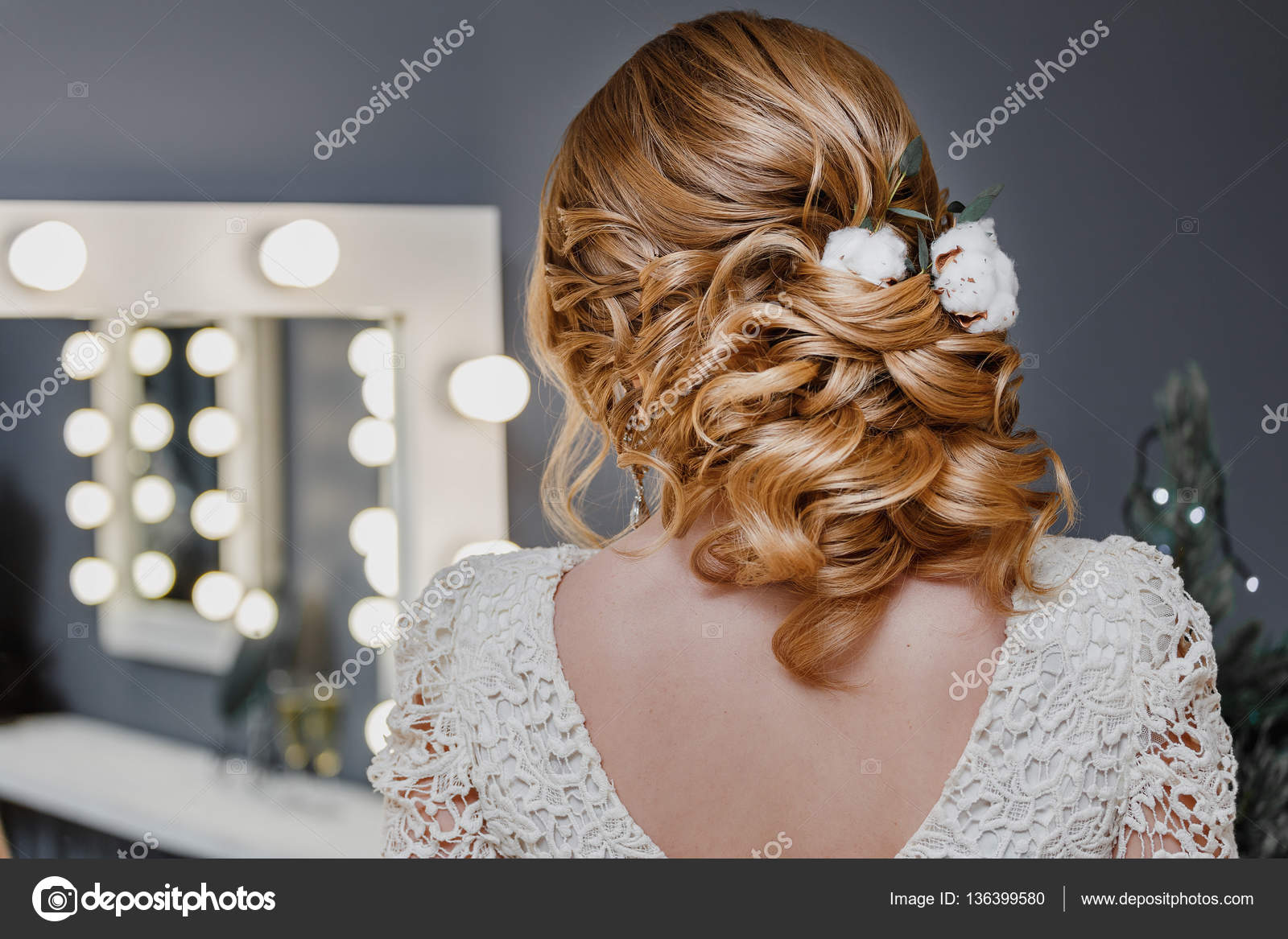 Young beautiful sandy haired woman with stylish hairdo with cotton flowers  in a beige dress preens near the mirror with lamps at beauty salon Stock  Photo by ©frantic00 136399580