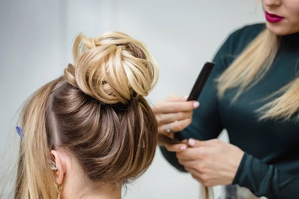 Hairdresser makes upper bun hairstyle close-up on brown hair of beautiful woman — Stock Photo, Image