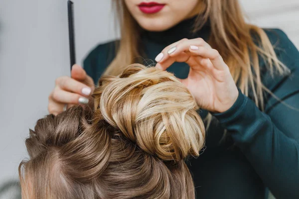 Hairdresser makes upper bun hairstyle close-up on brown hair of beautiful woman — Stock Photo, Image