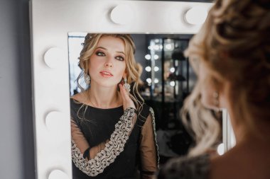 Genç güzel kadının akşam makyaj ve Güzellik Salonu lambalar ile aynaya bakarak takı ile yaratıcı saç modeli