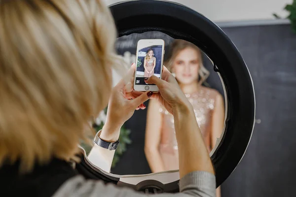 Uma mulher fotografa com smartphone o penteado no estúdio com uma lâmpada redonda — Fotografia de Stock