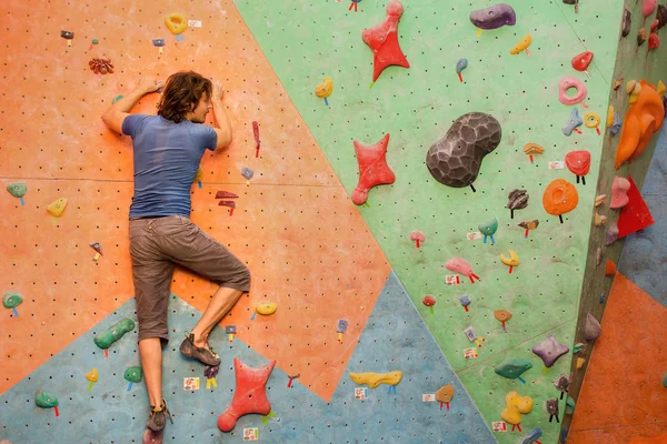 Young man climbing artificial boulder indoors, modern sport concept — Stock Photo, Image