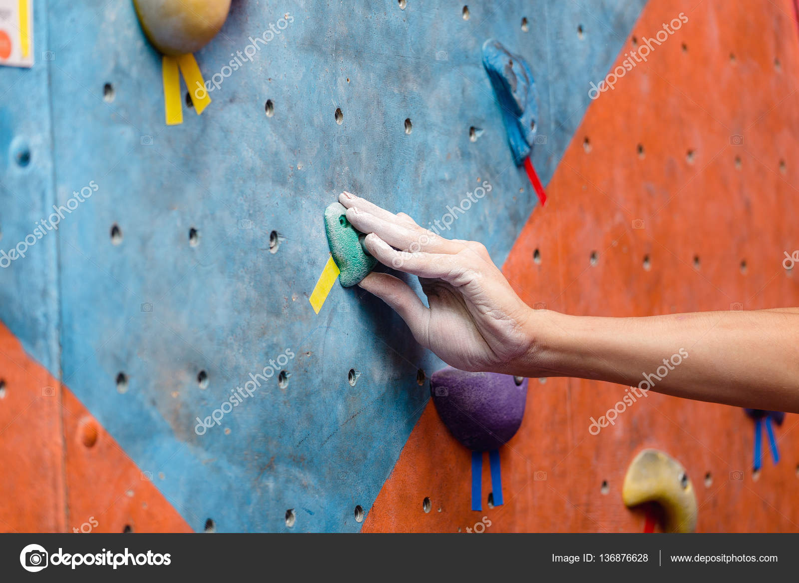Young man climbing indoor at artificial bouldering wall, close up of