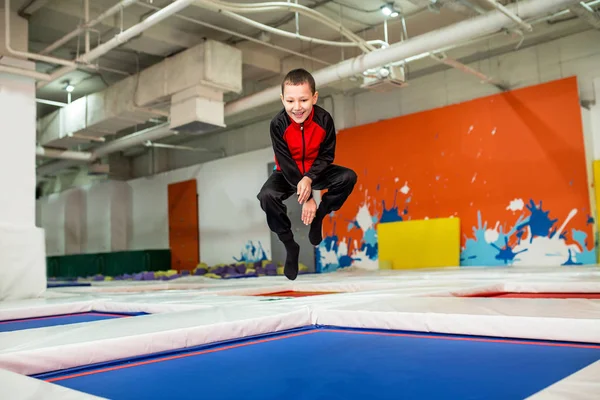 Pojken hoppar högt i randiga tights på stora studsmattan i kid sportcenter — Stockfoto