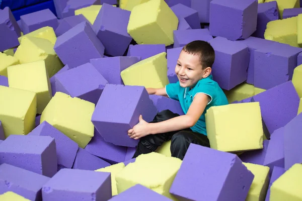 Barn pojke i skumgummi grop kasta färgade kuber — Stockfoto