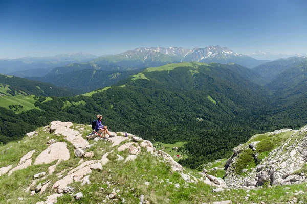 Mujer viajero en pantalones cortos en el verano está sentado en la cima de un acantilado — Foto de Stock