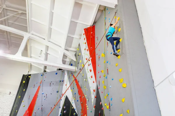 Счастливая спортсменка с альпинистским снаряжением висит на веревке у крытой скалолазания искусственной стены — стоковое фото