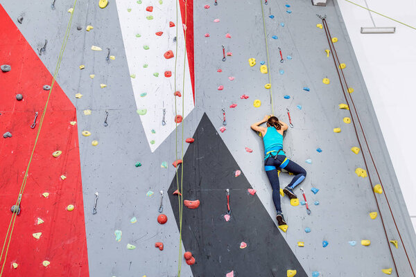 Young woman climbing up on practice wall at indoors gym, rear view