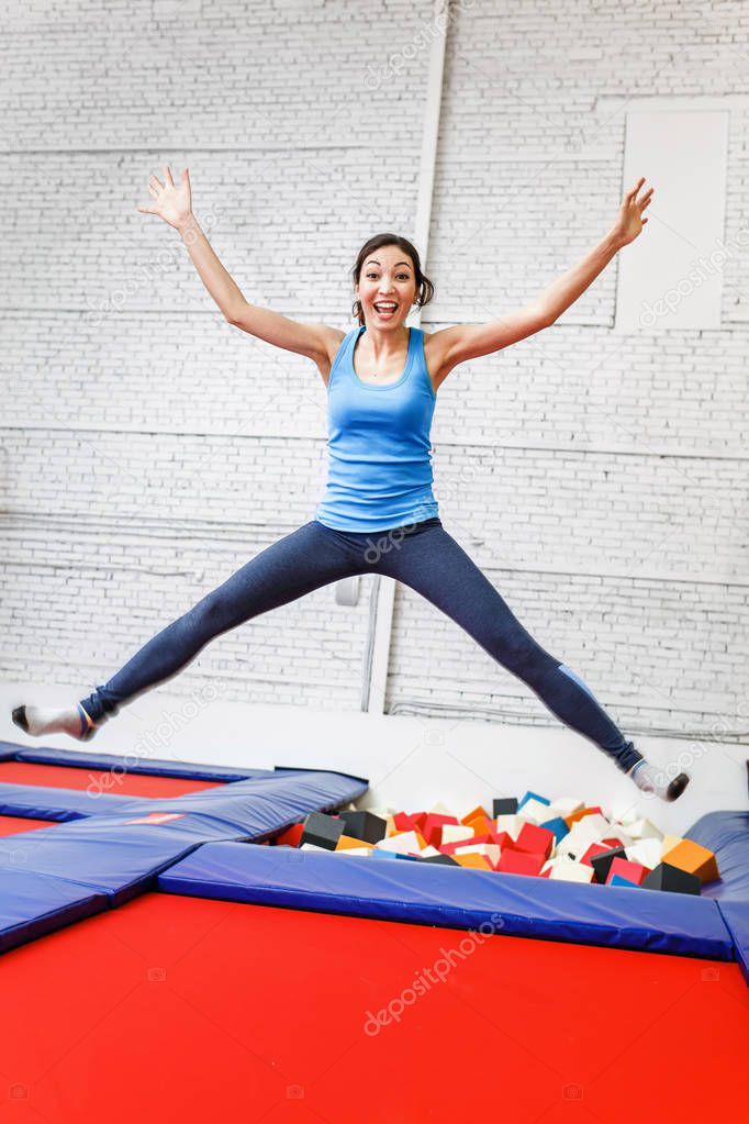 jumping young woman on the trampoline, white brick wall background