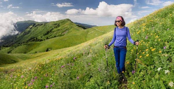 Dívka turistické procházky na stopě hill zelení s batohem a turistické hole — Stock fotografie