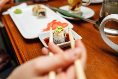 Kadın yemek suşi yemek çubukları ile bir restoranda alır.