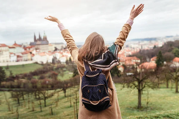 Turistické žena v plášti s batohem cestuje v parku Prahy, pohled zezadu — Stock fotografie