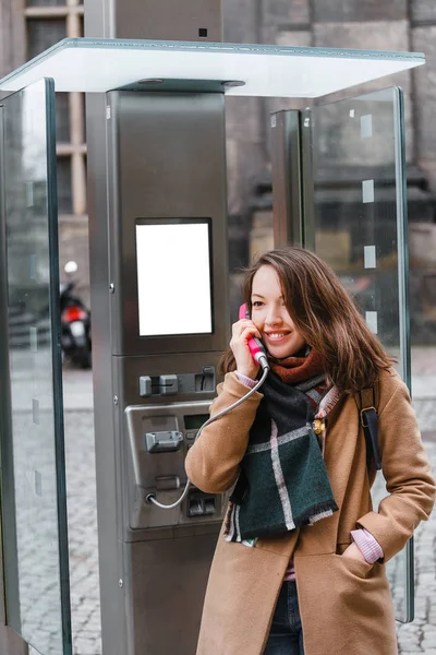 Retrato de mujer turista feliz y sonriente hablando en el moderno teléfono público en la calle de la ciudad, conexión telefónica durante un concepto de viaje — Foto de Stock