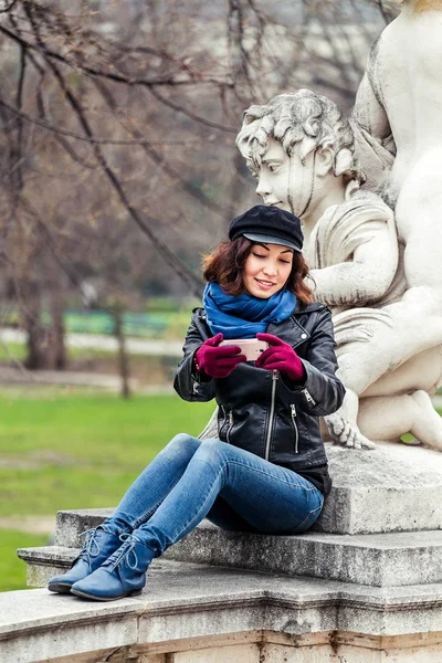 Fiatal női utas, így selfie a szobor Ámor szúró telefon, tavaszi kert és park — Stock Fotó