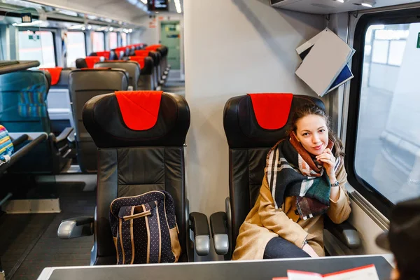 Mutlu kadın oturma arabaya tren ile seyahat ve tren istasyonunda pencereden görünüyor — Stok fotoğraf