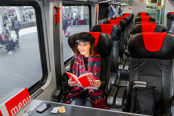 Mutlu kadın oturma arabaya tren ile seyahat ve tren istasyonunda pencereden görünüyor — Stok fotoğraf