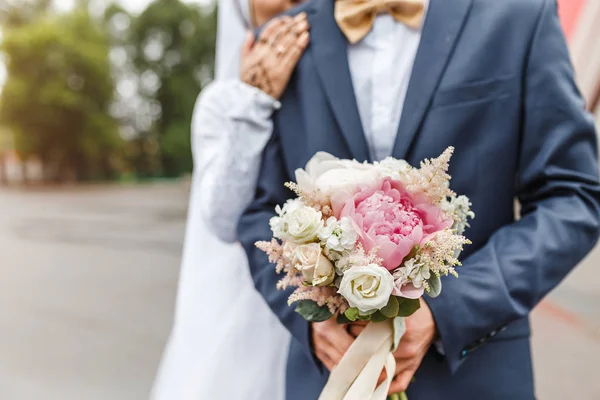 Bruden och brudgummen omfamna och hålla ett bröllop bukett av pastell blommor, närbild — Stockfoto