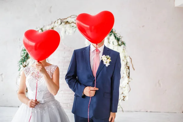 Novio feliz y novia cubierto sus caras con globos rojos en la fiesta de boda en el interior —  Fotos de Stock