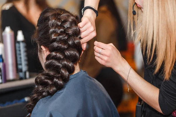 Cabeleireiro profissional fazendo um penteado de beleza com grande trança para o cabelo morena — Fotografia de Stock