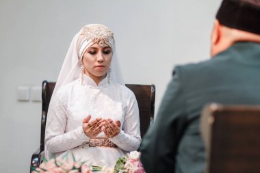Islamic woman in wedding dress praying in mosque with mullah clipart