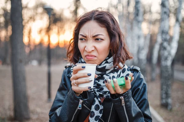 Шокированная женщина пробует отвратительный кофе или чай из одноразового кофе на открытом воздухе — стоковое фото