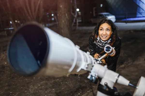 Жінка вночі дивиться на зоряне небо у великому професійному телескопі і посміхається — стокове фото