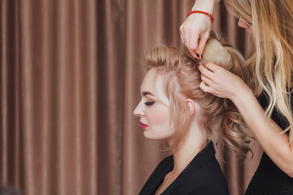 Cabeleireiro faz penteado da noite close-up no cabelo loiro de mulher de negócios no salão de beleza — Fotografia de Stock