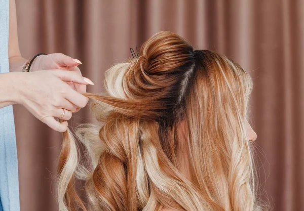 Hermosa chica rubia con el pelo largo haciendo un peinado de noche profesional en un salón de belleza — Foto de Stock