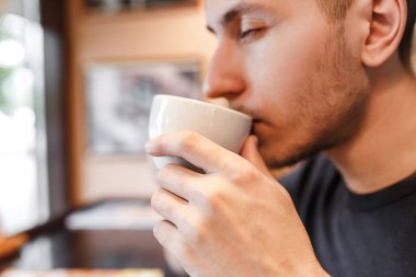 Genç bir adam bir kafede kahve veya çay bir bardaktan içer
