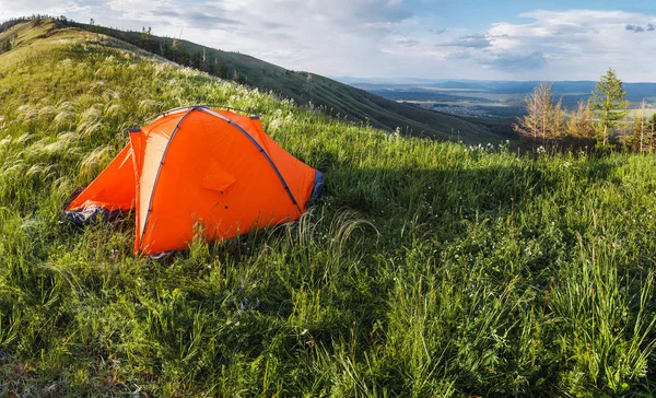 Tenda da trekking arancione in cima alla collina sotto l'erba fresca, concetto di svago all'aperto estivo — Foto Stock