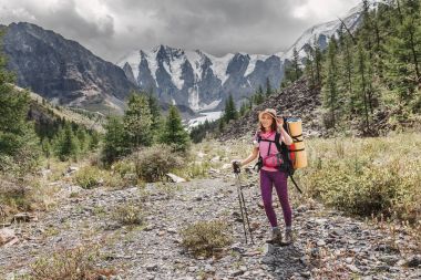 A woman with backpack travelling along river valley in mountains. Hiking and trekking concept clipart