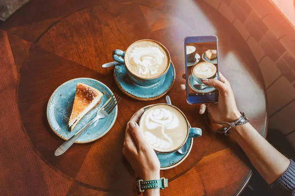 Крупный план мобильного смартфона в женских руках в кафе с чашкой кофе и тортом, плоский вид сверху — стоковое фото