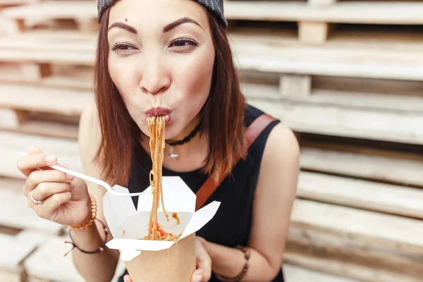Junge Frau isst asiatische Wok-Nudelküche aus der Take-away-Box am Straßenrand — Stockfoto
