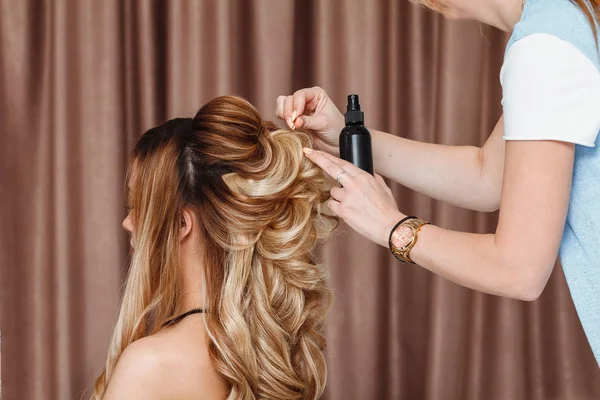 Vista de perto de um coiffeur de cabeleireiro faz o penteado da tarde ao modelo loiro no salão — Fotografia de Stock