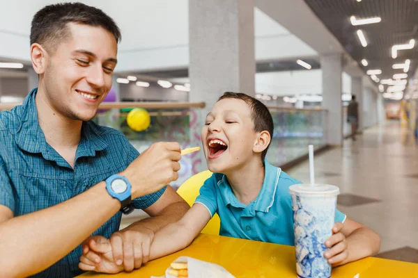 Küçük çocuk bir alışveriş merkezi ile onun babası ya da kardeşi kafede kızarmış bir fast food yeme